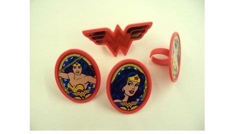 May include: Red Wonder Woman themed rings and emblem. The rings have an oval design with a portrait of Wonder Woman. The emblem is a red Wonder Woman logo. The rings and emblem are made of plastic.