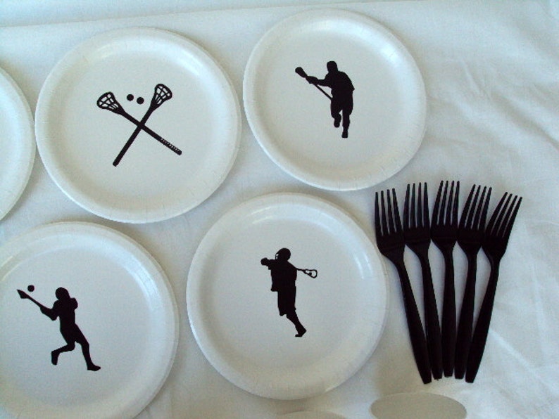 May include: White paper plates with black lacrosse-themed graphics. The plates feature crossed lacrosse sticks, and silhouettes of lacrosse players in action. Six black plastic forks are also included, perfect for a sports-themed party or event.