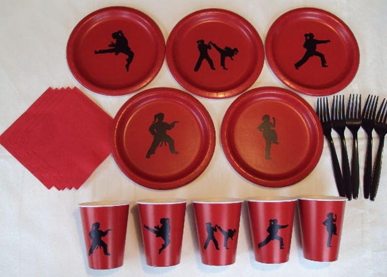 May include: Red and black paper plates and cups with a silhouette of a person doing a karate kick. There are also black plastic forks.