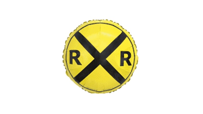 Op de afbeelding: Een gele, ronde ballon met een zwart spoorwegovergangssymbool en de letters "RR" aan weerszijden. De ballon is opgeblazen en heeft een metallic glans, wat suggereert dat hij van folie is gemaakt.