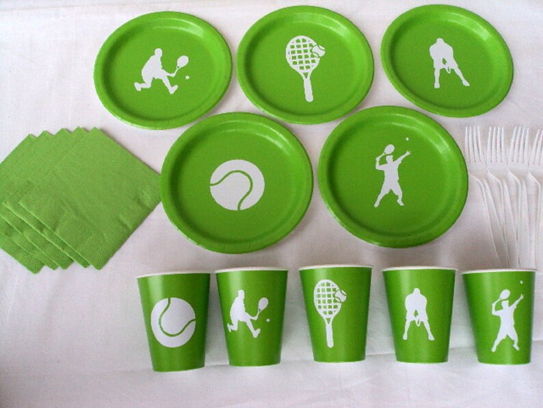 May include: Green paper plates and cups with white tennis-themed designs. The designs include tennis rackets, tennis balls, and tennis players. There are also green napkins and white plastic forks.