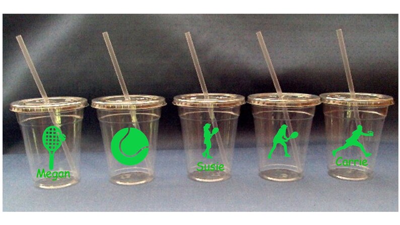 May include: Four clear plastic cups with green tennis-themed designs and straws. The cups are labeled "Megan", "Susie", "Carrie" and a tennis ball.