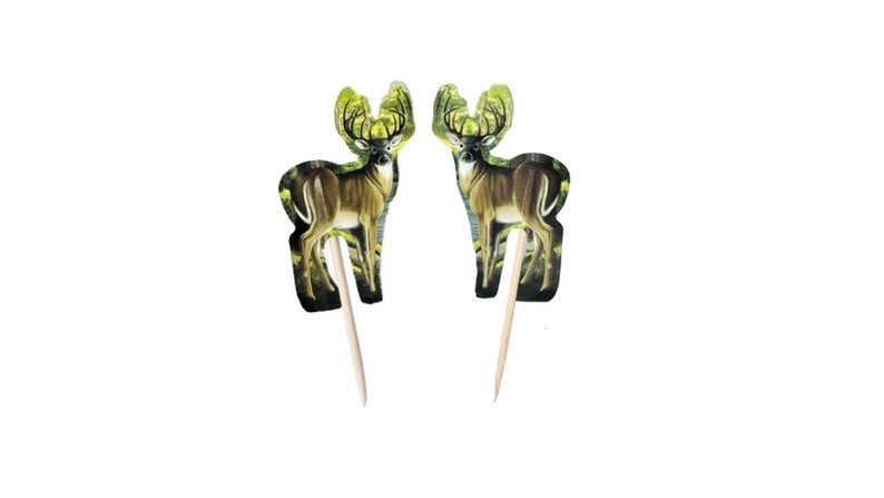 May include: Two brown deer cupcake toppers with green foliage backgrounds. The deer are standing on wooden skewers.