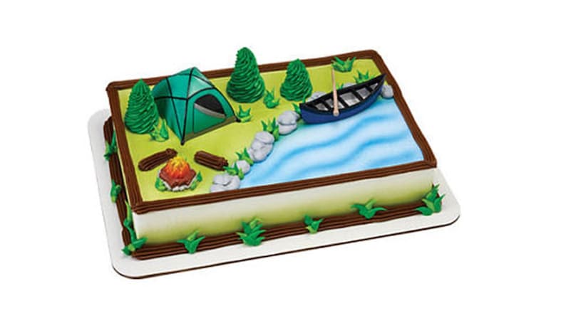 May include: A camping-themed cake decorated with a green tent, a blue canoe, a campfire, and green trees. The cake is on a white base with a brown border.