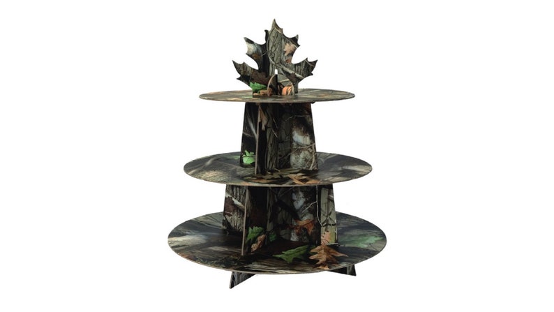 May include: Three-tiered cake stand with a camouflage pattern. The stand is made of cardboard and features a leaf-shaped topper.