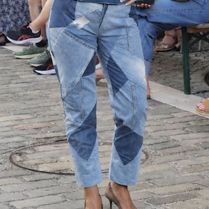 Könnte beinhalten: Blaue Jeanshose mit einem Patchwork-Design aus abwechselnd hell- und dunkelblauen Stoffbahnen in geometrischen Formen. Die Hose hat einen geradlinigen Schnitt, eine hohe Taille und sichtbare Nähte, die das gesamte Kleidungsstück strukturieren.