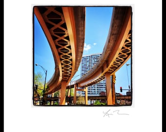 May include: A view of a city street with a large, multi-level overpass. The overpass is made of concrete and has a latticework design. The overpass is painted a light orange color. The overpass is in the foreground of the image, and a tall building is in the background.