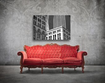 May include: A red velvet tufted sofa with ornate wooden legs sits in front of a black and white photograph of a city skyline.