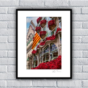 May include: A colourful building adorned with red roses, with a Catalan flag flying from the side. The building has a distinctive, whimsical design with arched windows and intricate details.