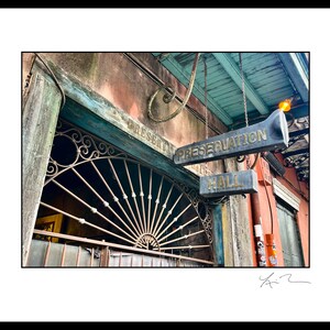 May include: A weathered building with a teal awning and a sign that reads "Preservation Hall". The sign is hanging from chains and has gold lettering. The building has a rusty metal gate with a decorative design.