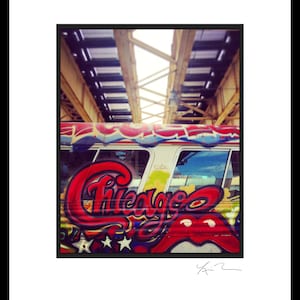 May include: A white bus with graffiti art featuring the word "Chicago" in red and black letters. The bus is parked under a bridge with a metal structure.