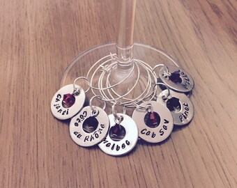 May include: Set of six silver wine glass charms with red glass beads. Each charm has a different wine varietal name engraved on it:  Cabernet Sauvignon, Pinot,  Valpolicella, Côtes du Rhône,  Chianti, and Merlot.