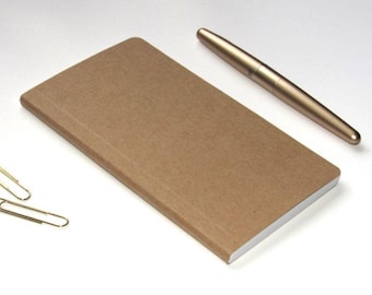 May include: A brown rectangular notebook with a gold pen and two gold paper clips on a white surface. The notebook is open, revealing white pages. The pen is metallic and cylindrical.