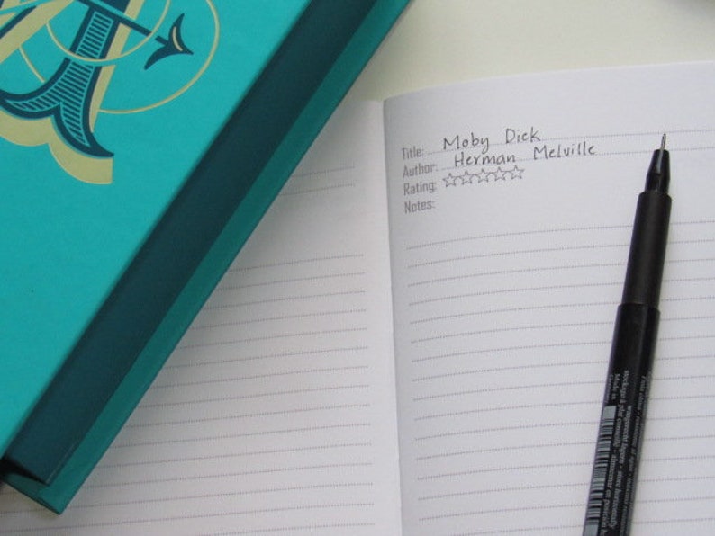 May include: An open notebook with the title "Moby Dick" and author Herman Melville, with a rating of three stars. A black pen rests on the lined pages. A teal book with gold accents is in the background.