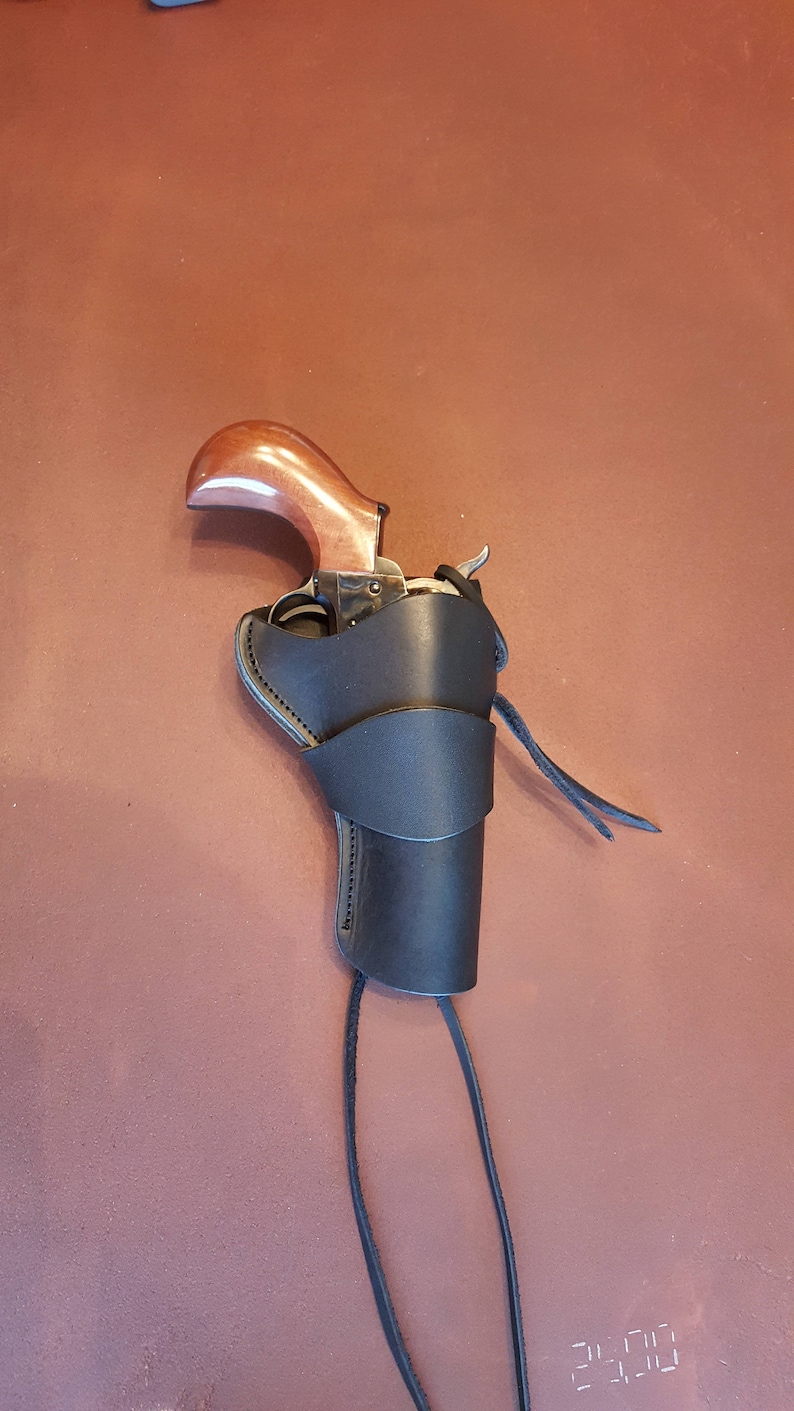 May include: A black leather holster with a brown wooden-handled revolver inside. The holster has a strap that goes around the leg and a long tie string.