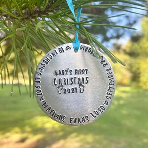 May include: Silver Christmas ornament with the text "Baby's First Christmas 2021" and the name "Maximus Evans Lord" with the date "September 6, 2021" and the time "8:53 PM".