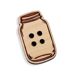 May include: A wooden button shaped like a mason jar with a brown outline. The button has four holes for sewing.
