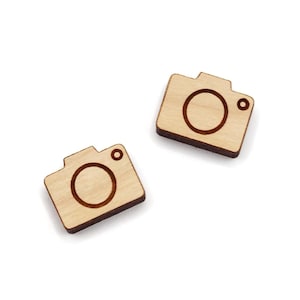 May include: Two small wooden camera-shaped ornaments. The ornaments are light brown and have a dark brown outline of a camera lens.