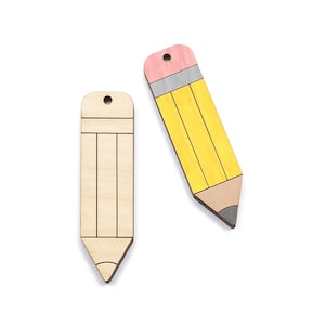 Peut inclure: Deux ornements en bois en forme de crayon, l'un peint en jaune avec des accents rose et gris, et l'autre laissé non peint.