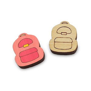 May include: Two wooden backpack-shaped cutouts. One is painted pink with a red interior and yellow accents, the other is natural wood. Both have a handle and a front pocket. Ideal for crafting or school-themed projects.