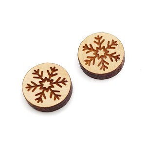 May include: Two wooden round ornaments with a snowflake design. The snowflakes are carved into the wood and have a brown color.