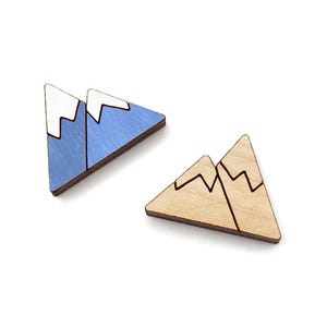 May include: Two wooden mountain-shaped earrings. One earring is painted blue with white snow peaks, and the other is natural wood with brown peaks.