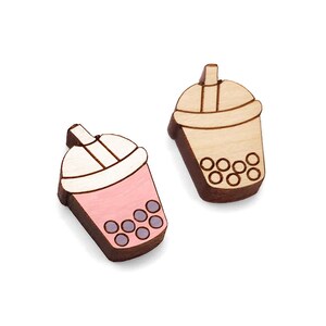 May include: Two wooden earrings shaped like boba tea cups. One is pink with purple boba pearls and the other is beige with brown boba pearls.