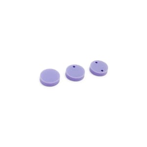 Peut inclure: Trois boutons ronds en silicone violet avec un nombre différent de trous. Les boutons sont disposés en rangée de gauche à droite.
