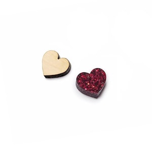 May include: Two heart-shaped objects are displayed. One heart is made of light-colored, smooth wood with a visible grain. The second heart is dark red and covered in reflective, sparkling glitter particles, creating a textured, shimmering surface.