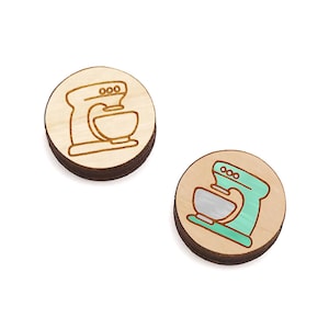 May include: Two wooden round ornaments with a laser-cut design of a stand mixer. One ornament is natural wood with a brown outline, the other is painted light green with a white outline.