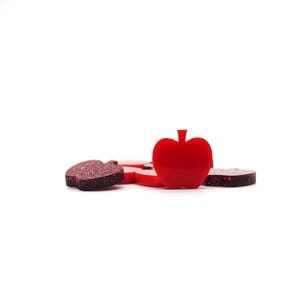 May include: A group of red glitter apple-shaped ornaments, one of which is larger and stands out in the center.