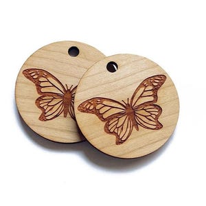 May include: Two round wooden ornaments with a laser-cut butterfly design. The butterflies are facing opposite directions and have intricate wing details.