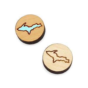 May include: Two wooden round earrings with a laser-cut outline of the Upper Peninsula of Michigan. One earring has a light blue fill inside the outline, while the other earring is unfilled.