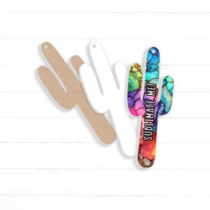 May include: A set of three unfinished wooden cactus shapes. One is brown, one is white, and one is decorated with colourful paint and the text "Sublimate Me!"