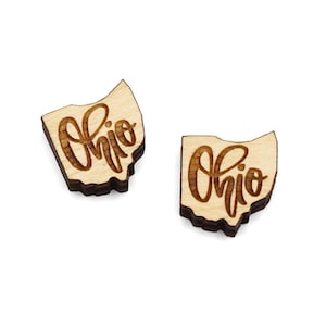 May include: A pair of wooden earrings shaped like the state of Ohio with the word "Ohio" written in cursive script.