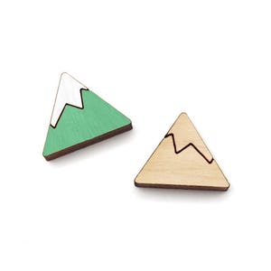 May include: Two wooden mountain-shaped ornaments. One is painted green with white snow on top. The other is natural wood with a black outline of the snow.