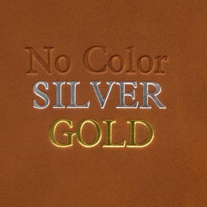 Puede incluir: Una muestra de cuero marr&oacute;n con las palabras "No Color", "SILVER" y "GOLD" en relieve en l&aacute;mina plateada y dorada.