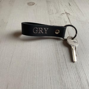 May include: Black leather keychain with a silver key ring and the name "GRY" engraved in silver lettering.
