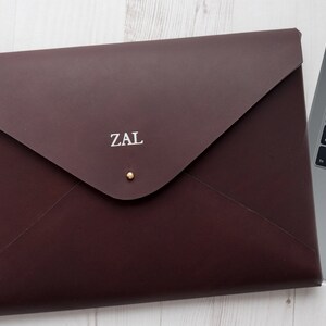 May include: A burgundy leather laptop sleeve with a gold button and the initials "ZAL" embossed in white.