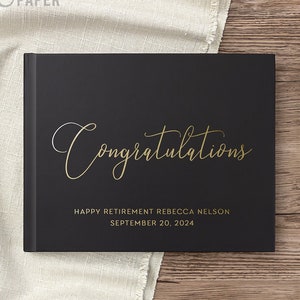May include: Black guest book with gold lettering that reads "Congratulations" and "Happy Retirement Rebecca Nelson September 20, 2024".