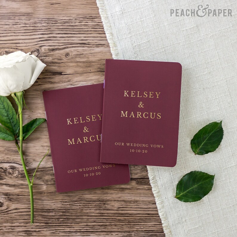 May include: Two burgundy wedding vow books with gold lettering. The top book says "Kelsey & Marcus" and "Our Wedding Vows 10-10-20". The bottom book says "Kelsey & Marcu" and "Our Wedding Vows 10-10-20".