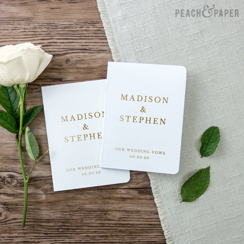 May include: Two white wedding vow books with gold lettering. The top book says "Madison & Stephen" and "Our Wedding Vows 06-20-20". The bottom book says "Madison & Stephen" and "Our Wedding 06-20-20".