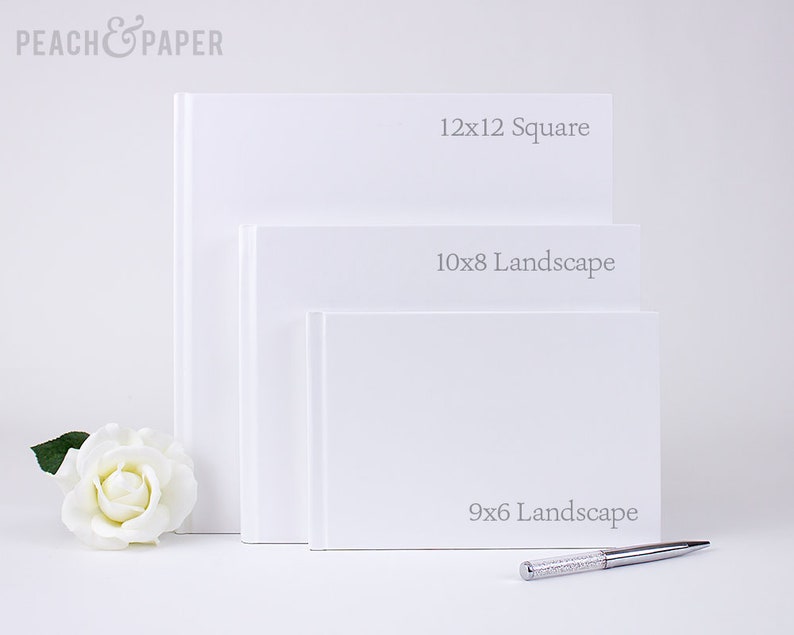 May include: Three white blank books of varying sizes, labeled "12x12 Square", "10x8 Landscape", and "9x6 Landscape". A white rose and a silver pen with crystal accents are also present. The books are stacked, with the largest on top.