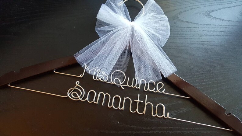 Pu&ograve; includere: Un appendiabiti in legno marrone scuro con le parole "Mrs Quince Samantha" in filo d'argento. Un fiocco di tulle bianco &egrave; attaccato in cima. Per un'occasione speciale.