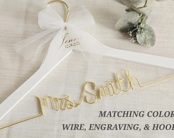 May include: A white wooden clothes hanger featuring a gold wire script reading Mrs. Smith, a white tulle bow tied to the gold hook, and the engraved name Jenna with the date 12.24.2025. Text on the image reads MATCHING COLOR WIRE, ENGRAVING, & HOOK.