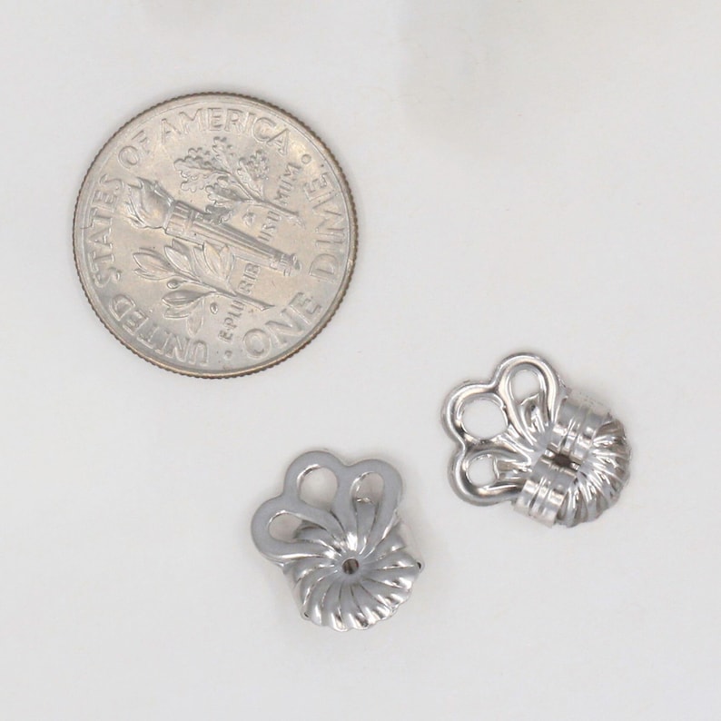 Peut inclure: Deux fermoirs de boucles d'oreilles en m&eacute;tal argent&eacute; avec un bord sup&eacute;rieur festonn&eacute; en forme de c&oelig;ur et une base circulaire nervur&eacute;e. Une pi&egrave;ce de dix cents am&eacute;ricaine est plac&eacute;e &agrave; gauche pour donner une &eacute;chelle de taille.