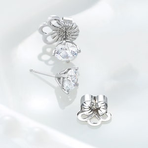 Peut inclure: Une paire de boucles d'oreilles &agrave; clous argent&eacute;es avec des pierres rondes, transparentes et facett&eacute;es mont&eacute;es sur des paniers &agrave; quatre griffes. Deux fermoirs m&eacute;talliques en forme de fleur sont pr&eacute;sent&eacute;s d&eacute;tach&eacute;s des tiges.