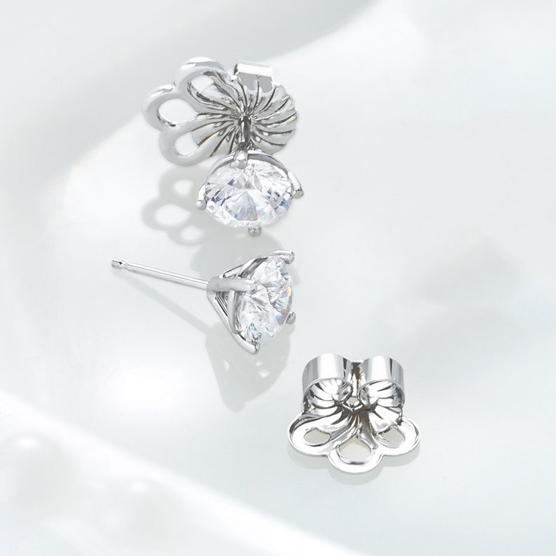 Peut inclure: Une paire de boucles d'oreilles &agrave; clous argent&eacute;es avec des pierres rondes, transparentes et facett&eacute;es mont&eacute;es sur des paniers &agrave; quatre griffes. Deux fermoirs m&eacute;talliques en forme de fleur sont pr&eacute;sent&eacute;s d&eacute;tach&eacute;s des tiges.
