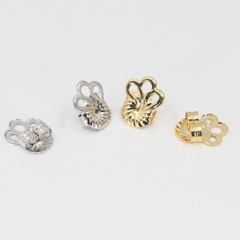 Peut inclure: Quatre fermoirs de boucles d'oreilles dispos&eacute;s en rang&eacute;e, comprenant deux pi&egrave;ces argent&eacute;es et deux pi&egrave;ces dor&eacute;es. Chaque fermoir pr&eacute;sente une forme festonn&eacute;e en fleur avec une ouverture centrale et une surface nervur&eacute;e textur&eacute;e.