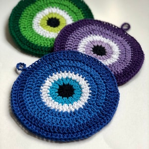 May include: Three crocheted evil eye wall hangings in blue, purple, and green. Each hanging features a white circle with a black pupil in the center.